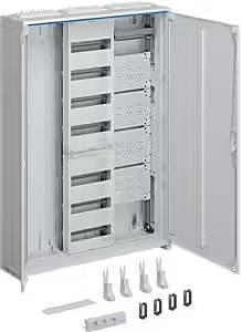 Otevřená rozváděčová skříň, prázdná s několika poličkami a příslušenstvím ležícím na zemi před ní. Vhodná pro elektroinstalace.