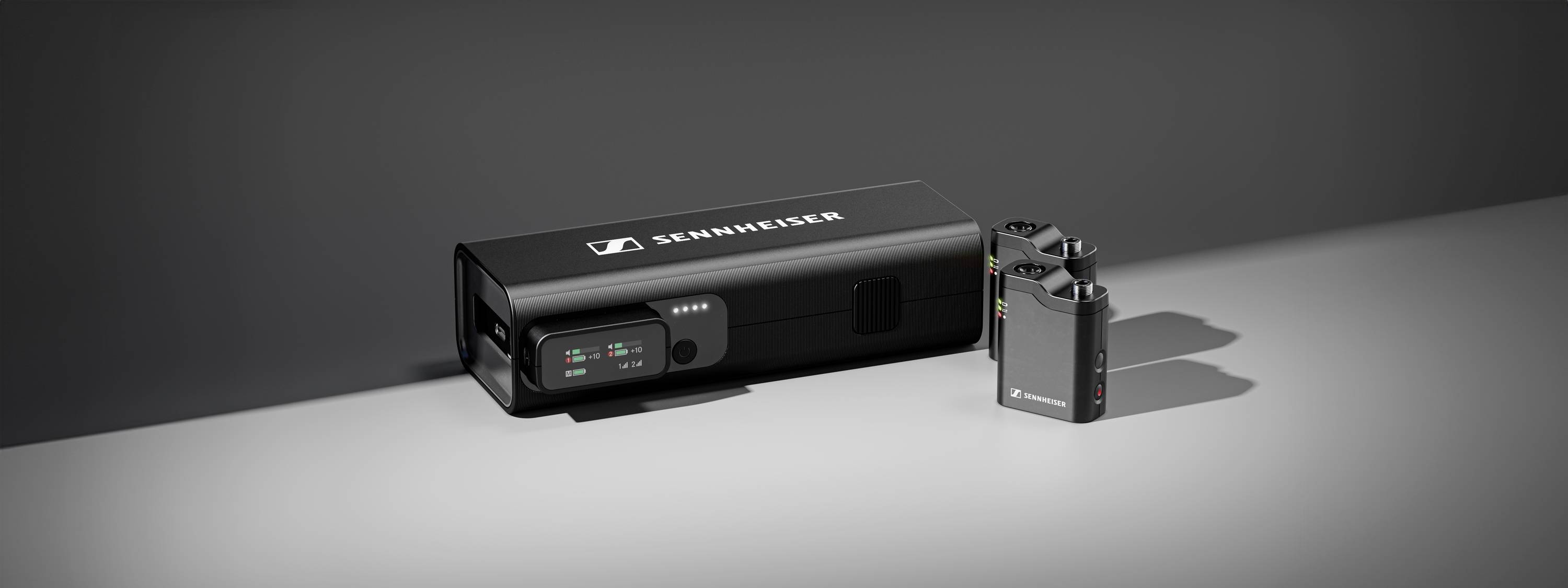 Bezdrátová mikrofonní sada Sennheiser. Obsahuje jeden přijímač a dva kompaktní vysílače s LED indikátory. Moderní design na šedém pozadí.