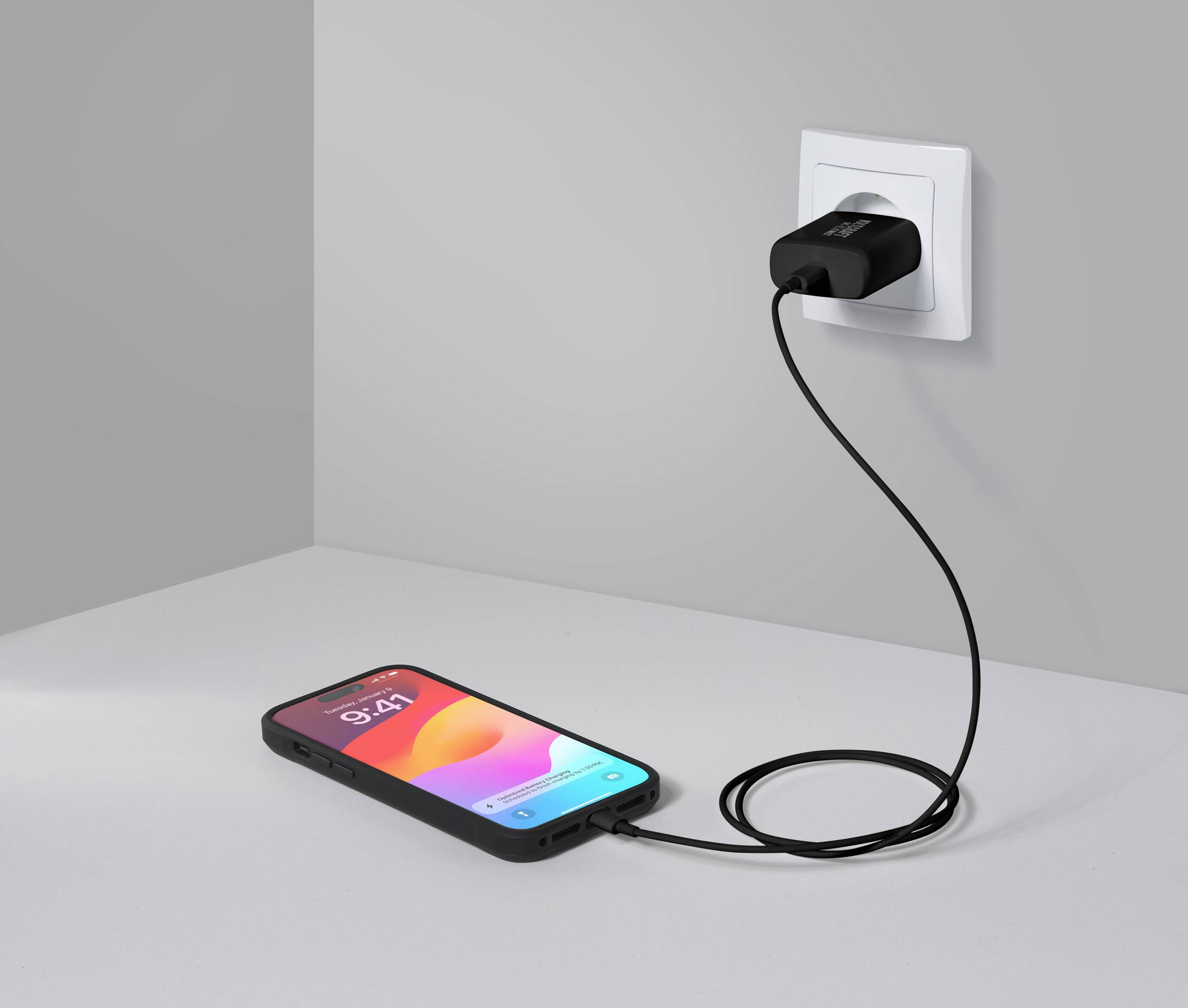 Smartphone leží na stole a je nabíjeno prostřednictvím kabelu do síťové zásuvky.