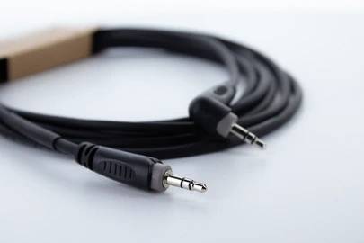 Černý audiokabel se dvěma jack konektory na bílém pozadí, který se často používá k propojení audio zařízení.