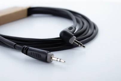 Černý audioкabel se dvěma 3,5mm jack konektory, svinutý a ležící na bílém pozadí.