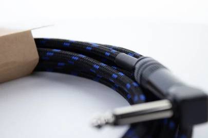 Černý audiokabel s modrými značkami a kovovým konektorem na bílém pozadí, částečně zabalený v kartónové krabici.