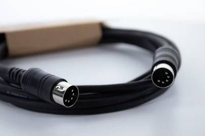 Černý kabel se dvěma kulatými DIN konektory na koncích, položený na bílém pozadí.