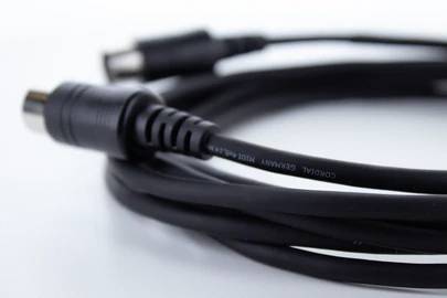 Černý koaxiální kabel se dvěma konektory na bílém povrchu. Často se používá pro připojení televizorů.
