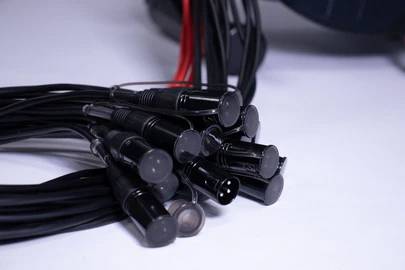 Několik černých audio kabelů s různými konektory leží na světlém povrchu. Některé jsou navzájem propletené.