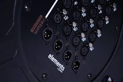 'Detailní záběr černého audio zařízení s několika XLR konektory, očíslovanými od 13 do 16. Bílý nápis značky 'elements' je viditelný.'