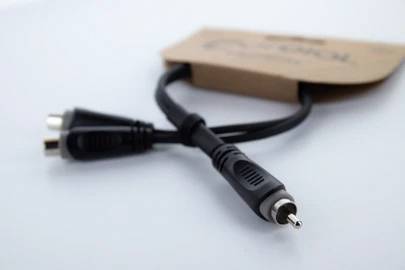 'RCA-na-duální rozbočovací kabel umístěný na stole. Kabel má jeden zástrčkový konektor, který se rozdvojuje do dvou samostatných výstupů.'