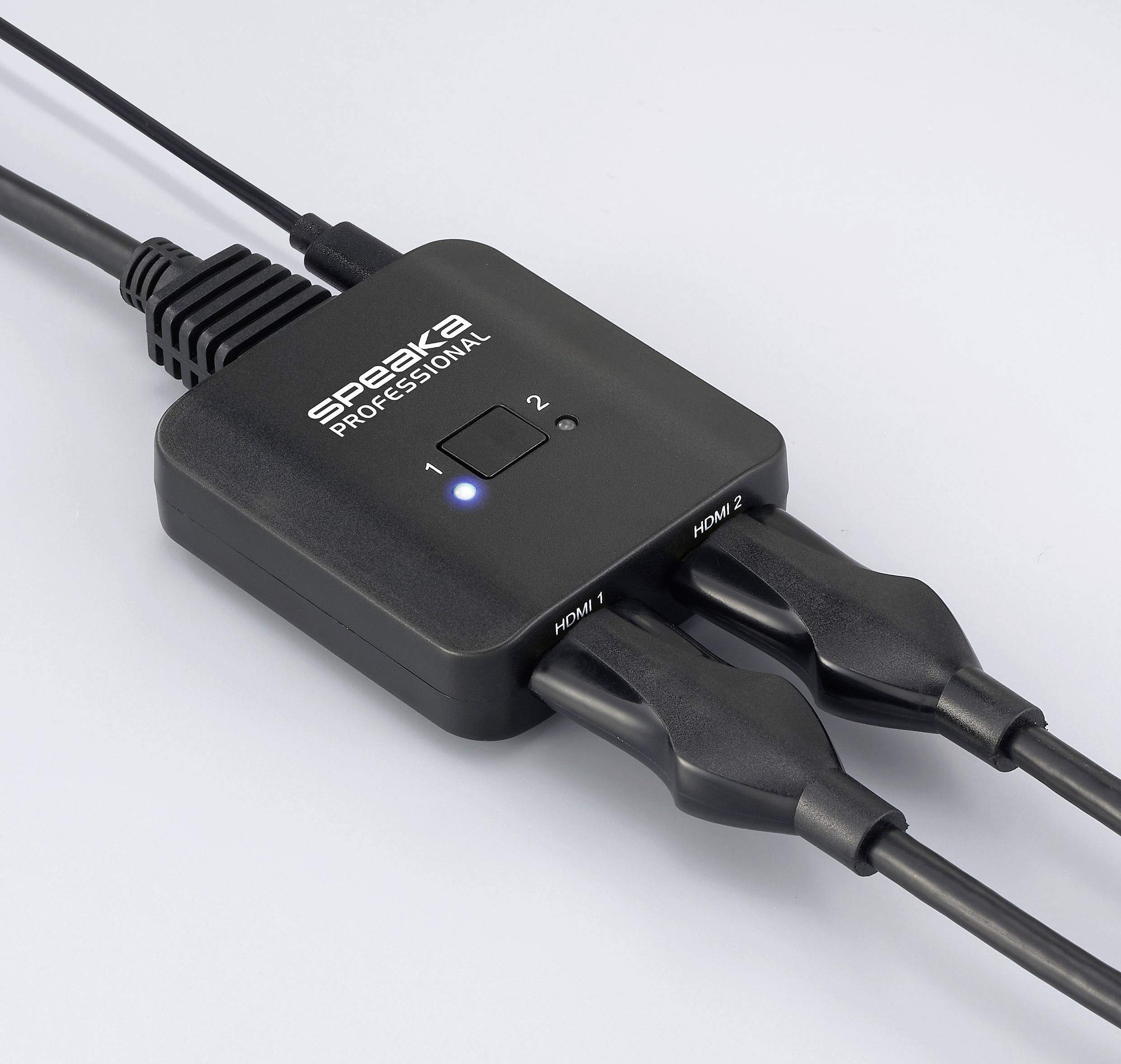 HDMI přepínač s nápisem 'SPEAKA PROFESSIONAL', se dvěma zapojenými HDMI kabely a osvětleným indikátorem pro vstup 1.