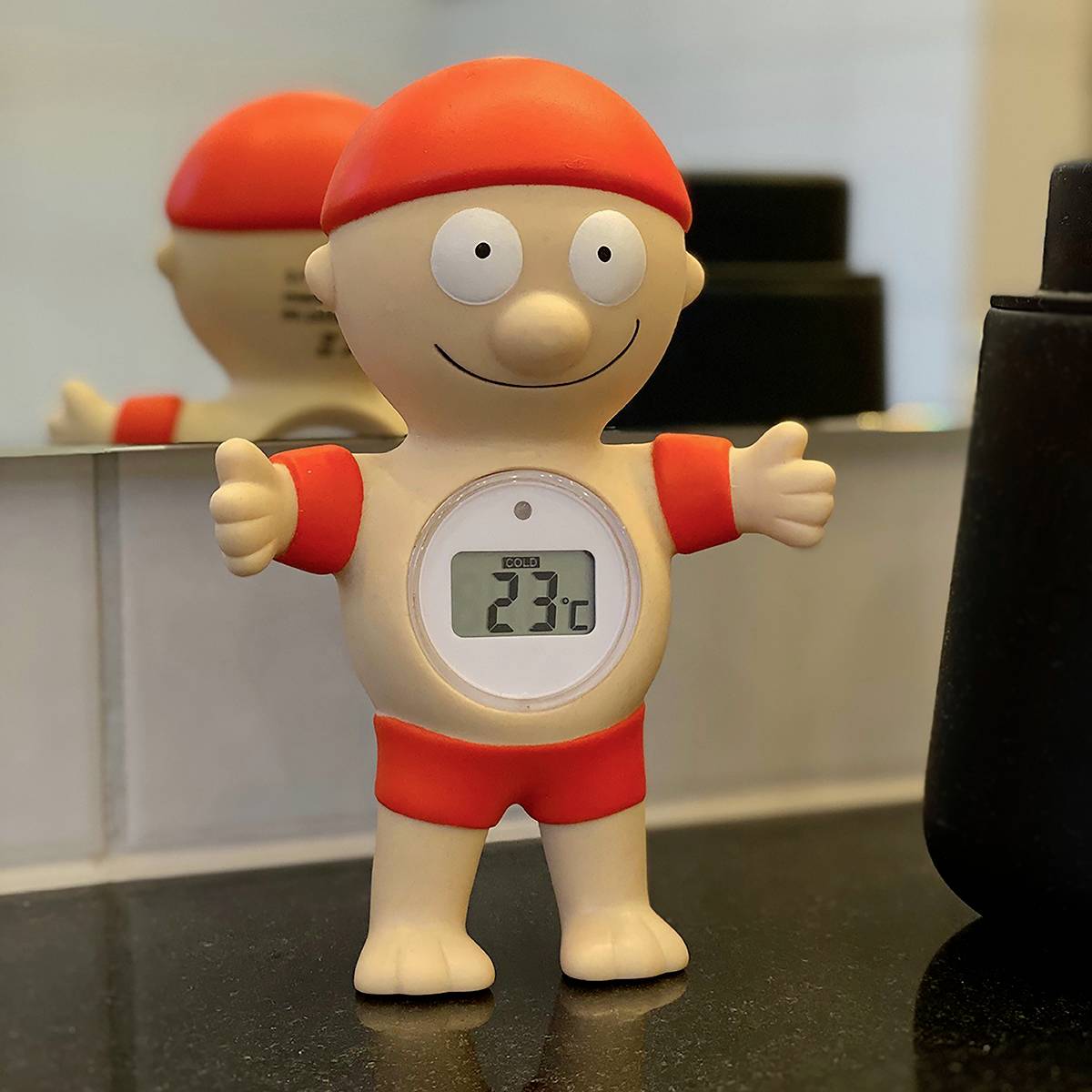 Usměvavá postava v červeném oblečení ukazuje na vestavěném malém displeji teplotu 23°C.