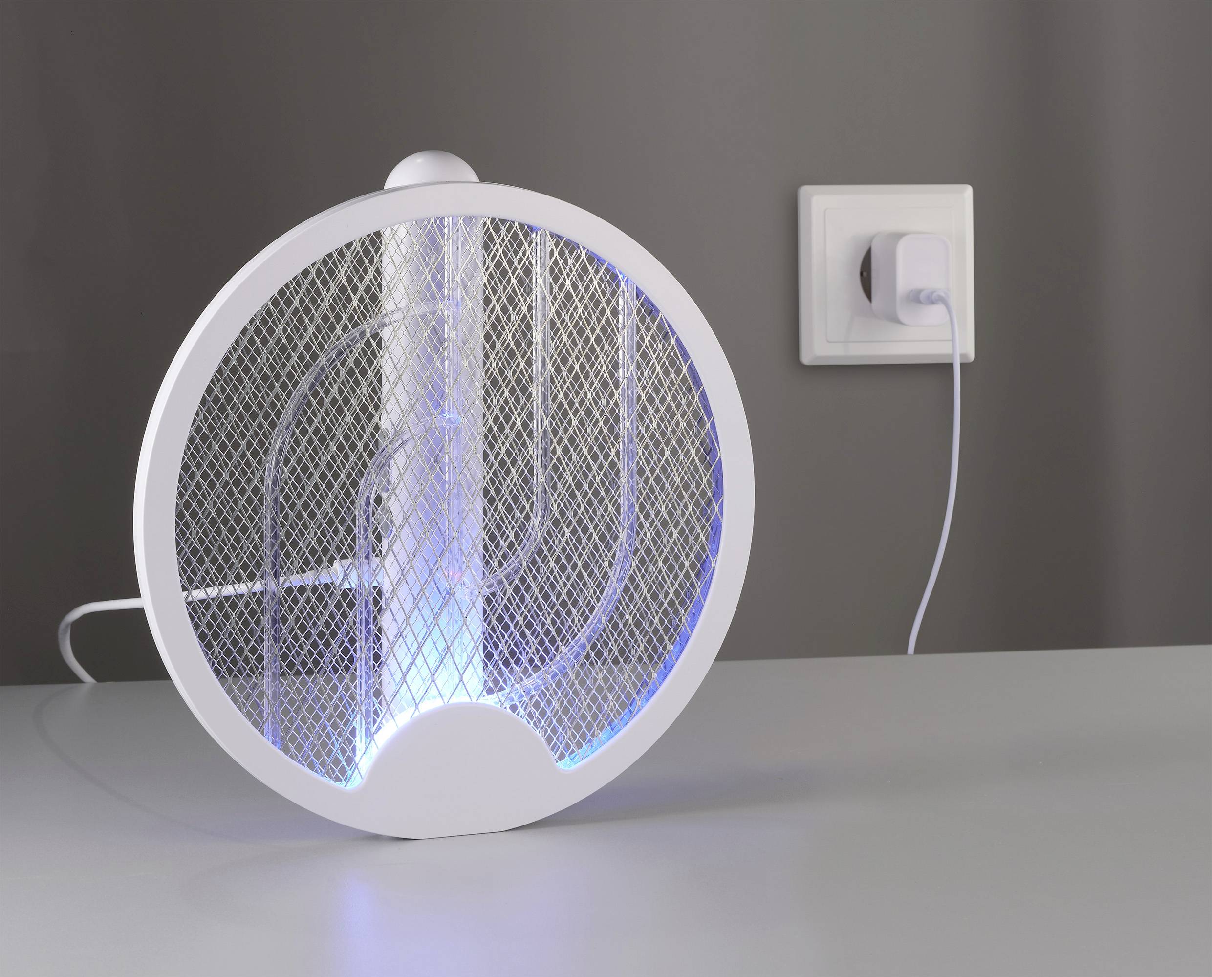 Elektrický lapač hmyzu se modrým světlem stojí na stole a je připojen kabelem do elektrické zásuvky.