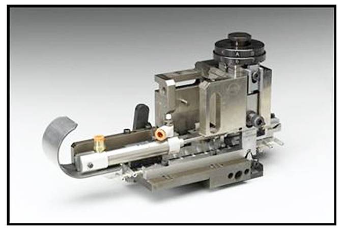 Mechanické zařízení z kovu, pravděpodobně specializovaný stroj nebo nástroj, umístěné na neutrálním pozadí.