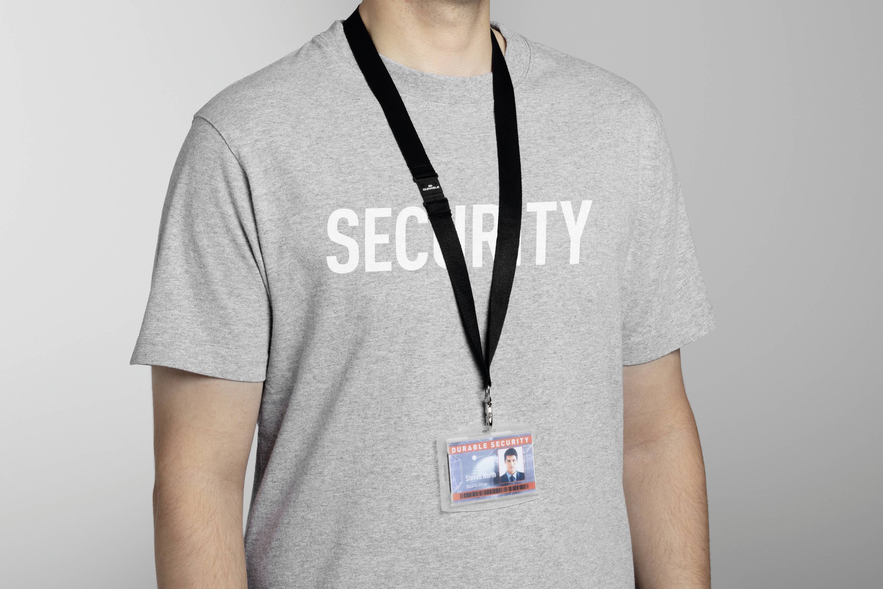 Osoba v šedém tričku s nápisem 'SECURITY', která má na krku černou šňůrku s identifikačním průkazem.