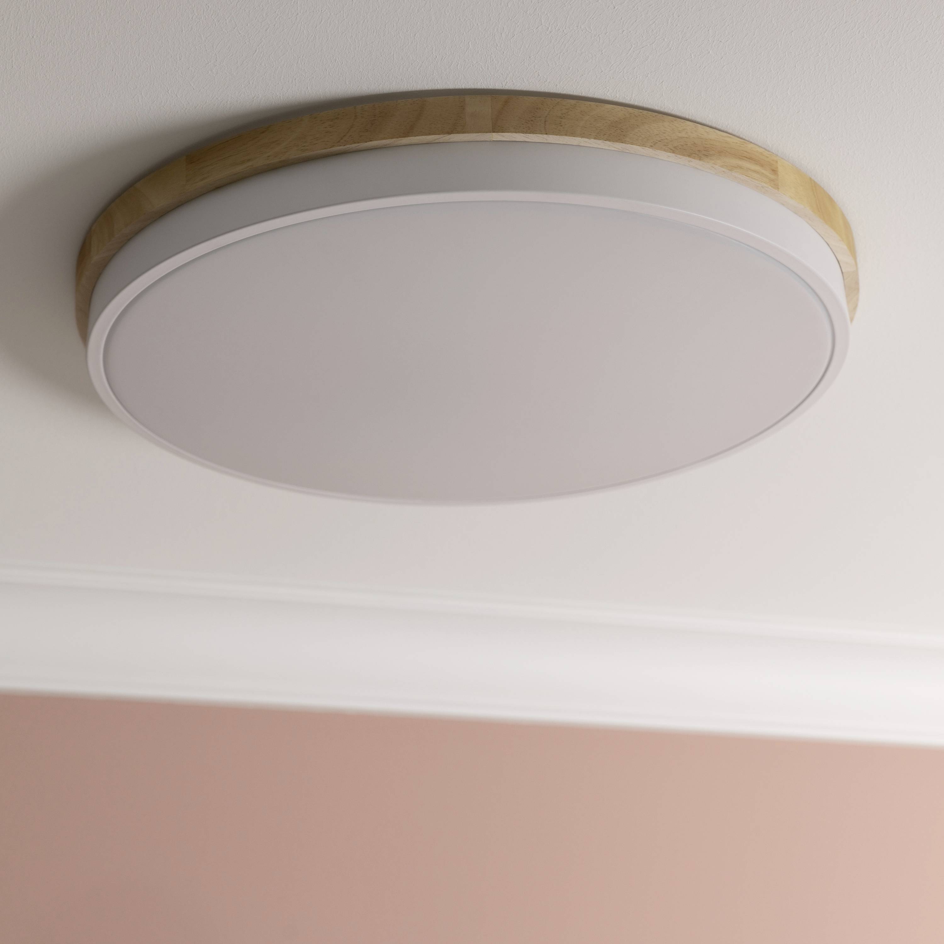 Moderní kulatá stropní lampa s dřevěnými detaily v místnosti s růžovými stěnami.