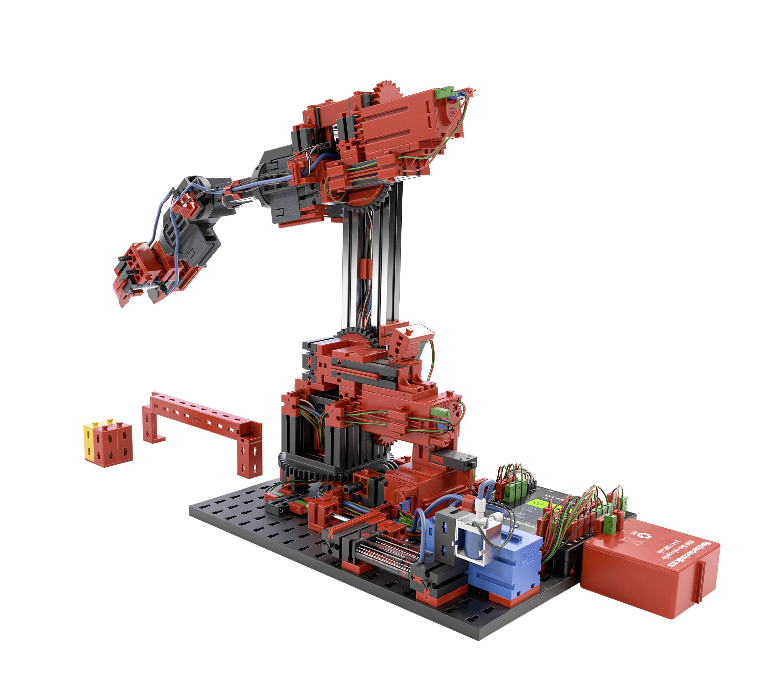 Červená a černá robotická paže ze stavebnice, částečně propojená kabely, stojí na základní desce. Vlevo vedle ní leží další komponenty.