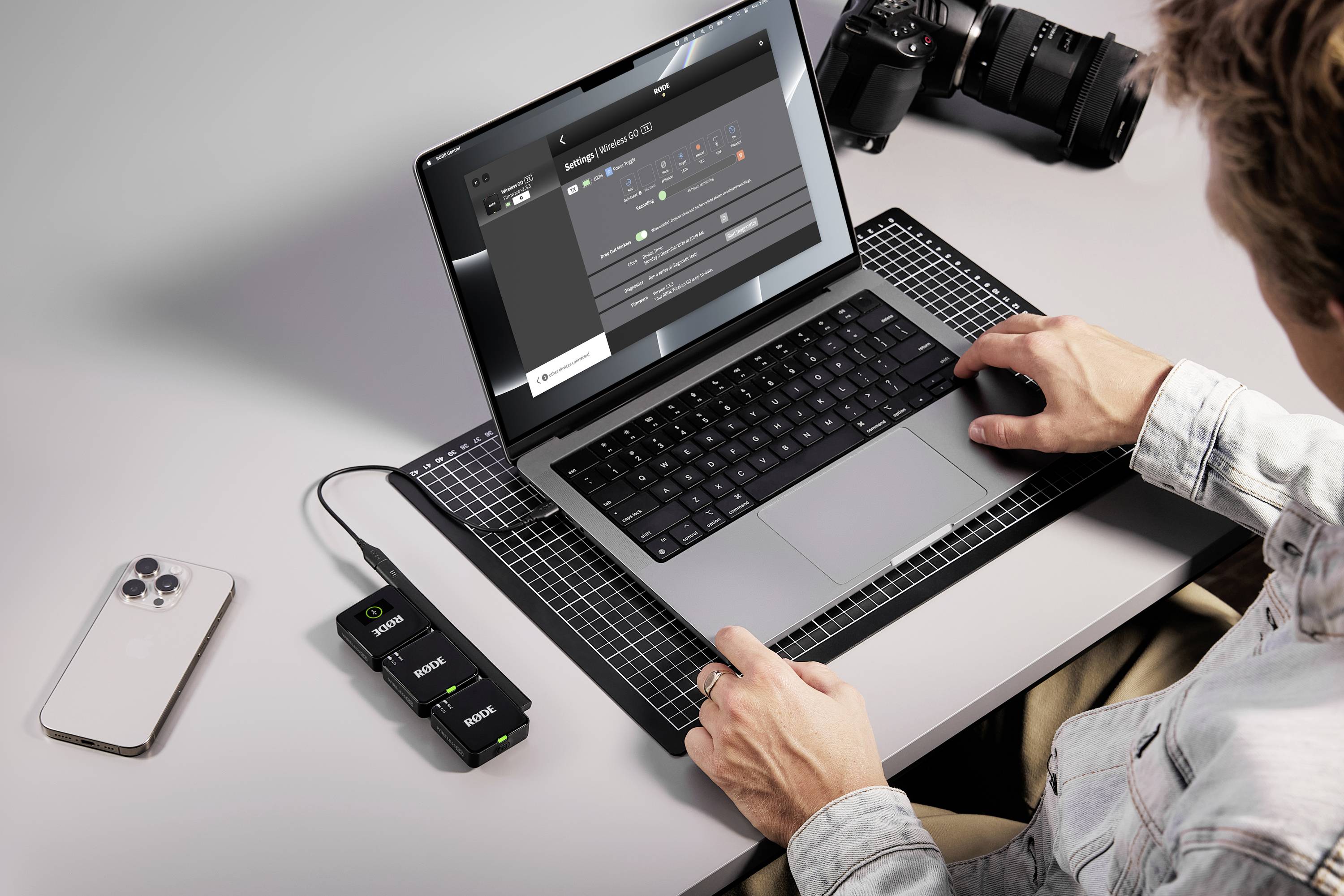 Osoba pracuje na notebooku s editačním softwarem pro úpravu obrázků. Vedle ní leží smartphone, fotoaparát a nabíjecí zařízení.