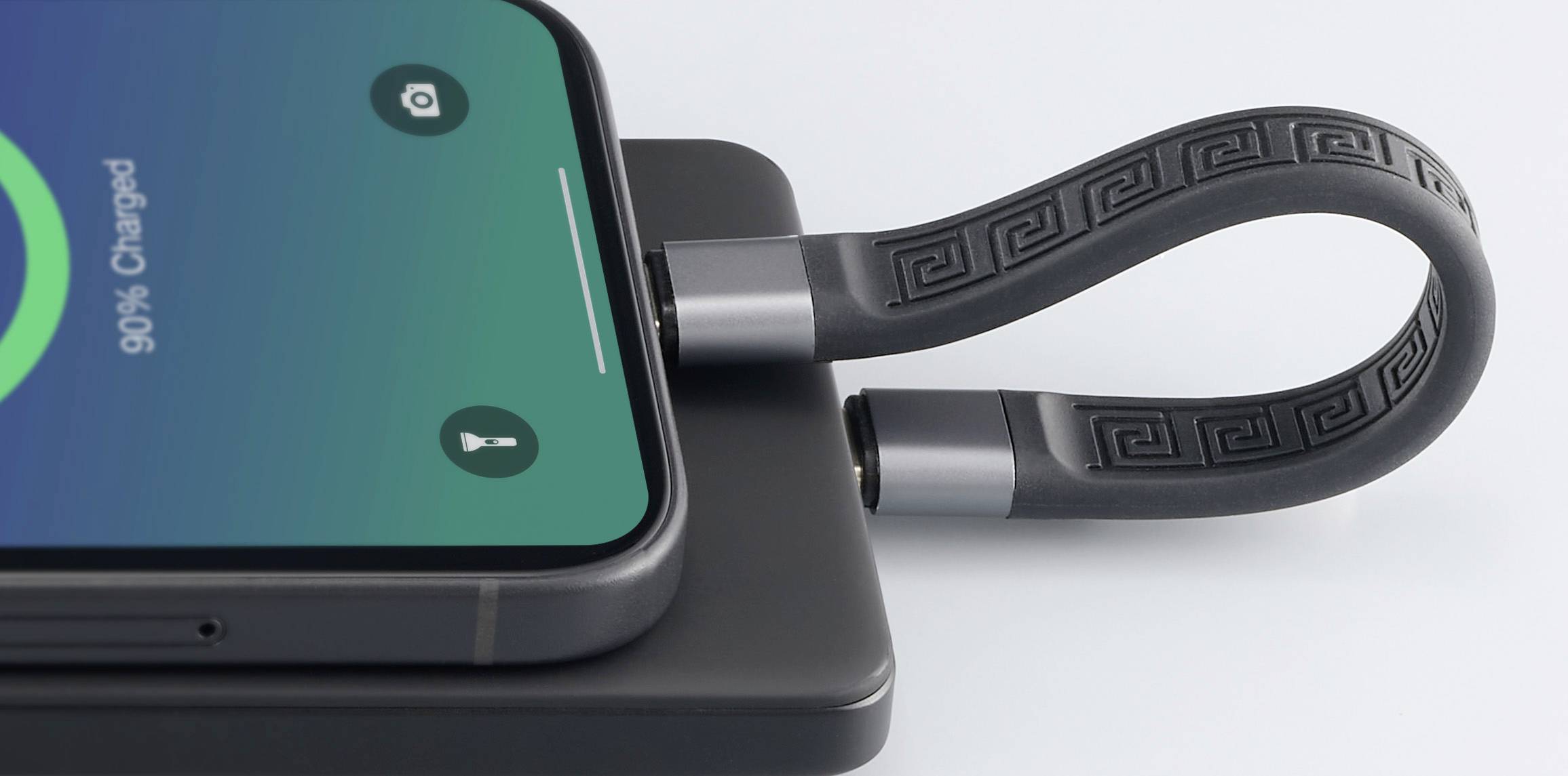 Mobilní telefon s nabíjecím kabelem leží na nabíjecí podložce. Na displeji je zobrazeno '90% nabito'. Kabel má moderní design.