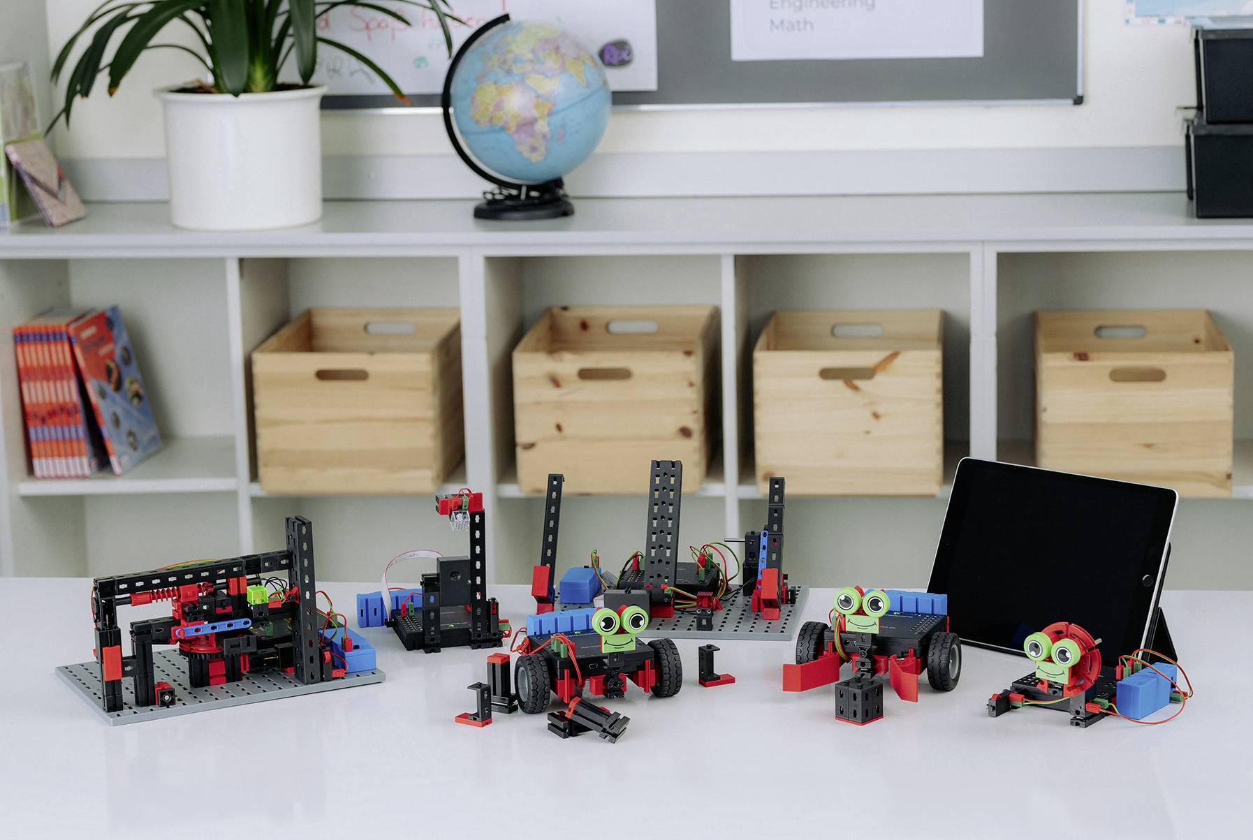 Robotické sady a tablet na stole ve třídě; vzdělávací prostředí pro robotiku a technologie.