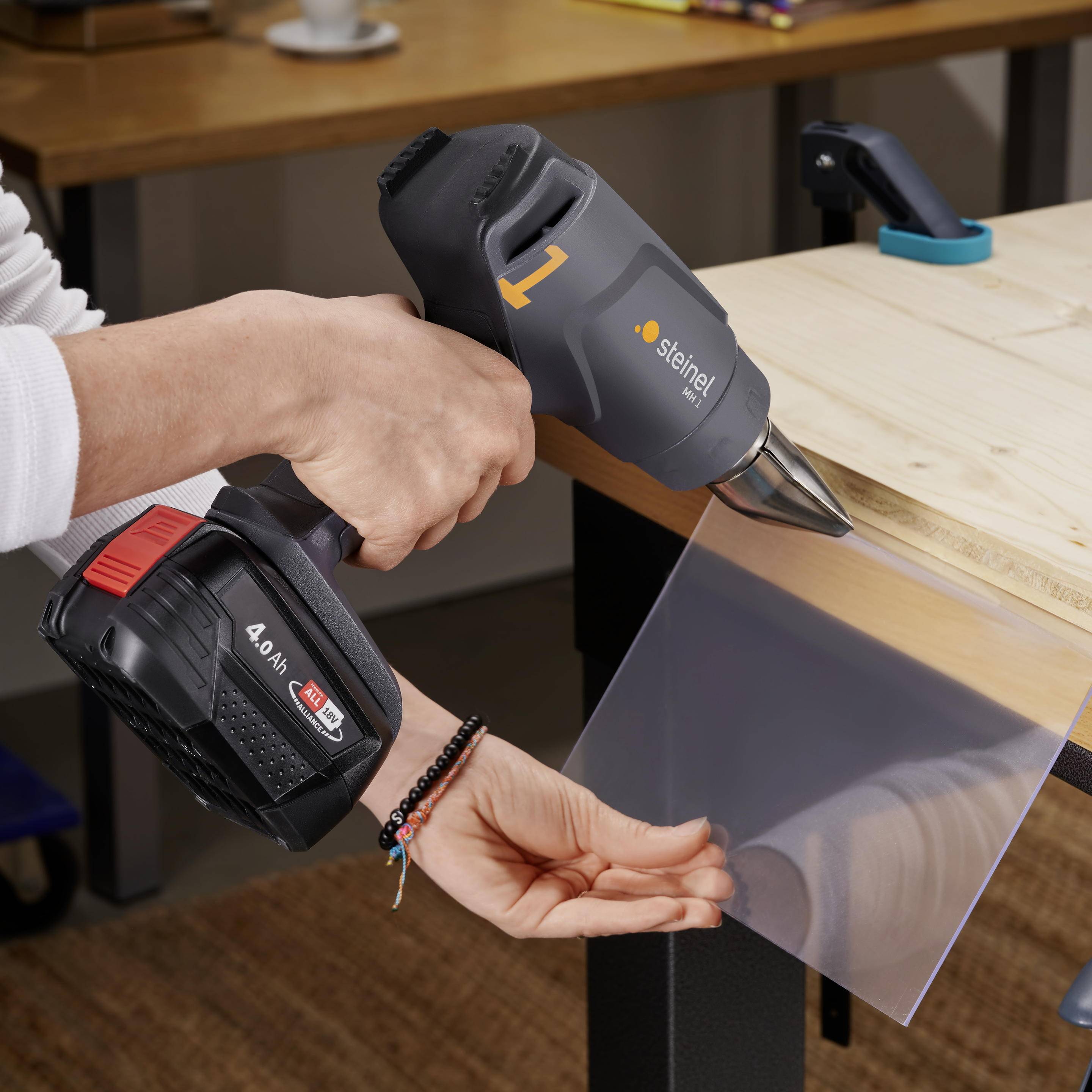 Jedna osoba řeže plastový materiál elektrickým nástrojem. Zařízení je šedo-oranžové barvy a nachází se v dílně.