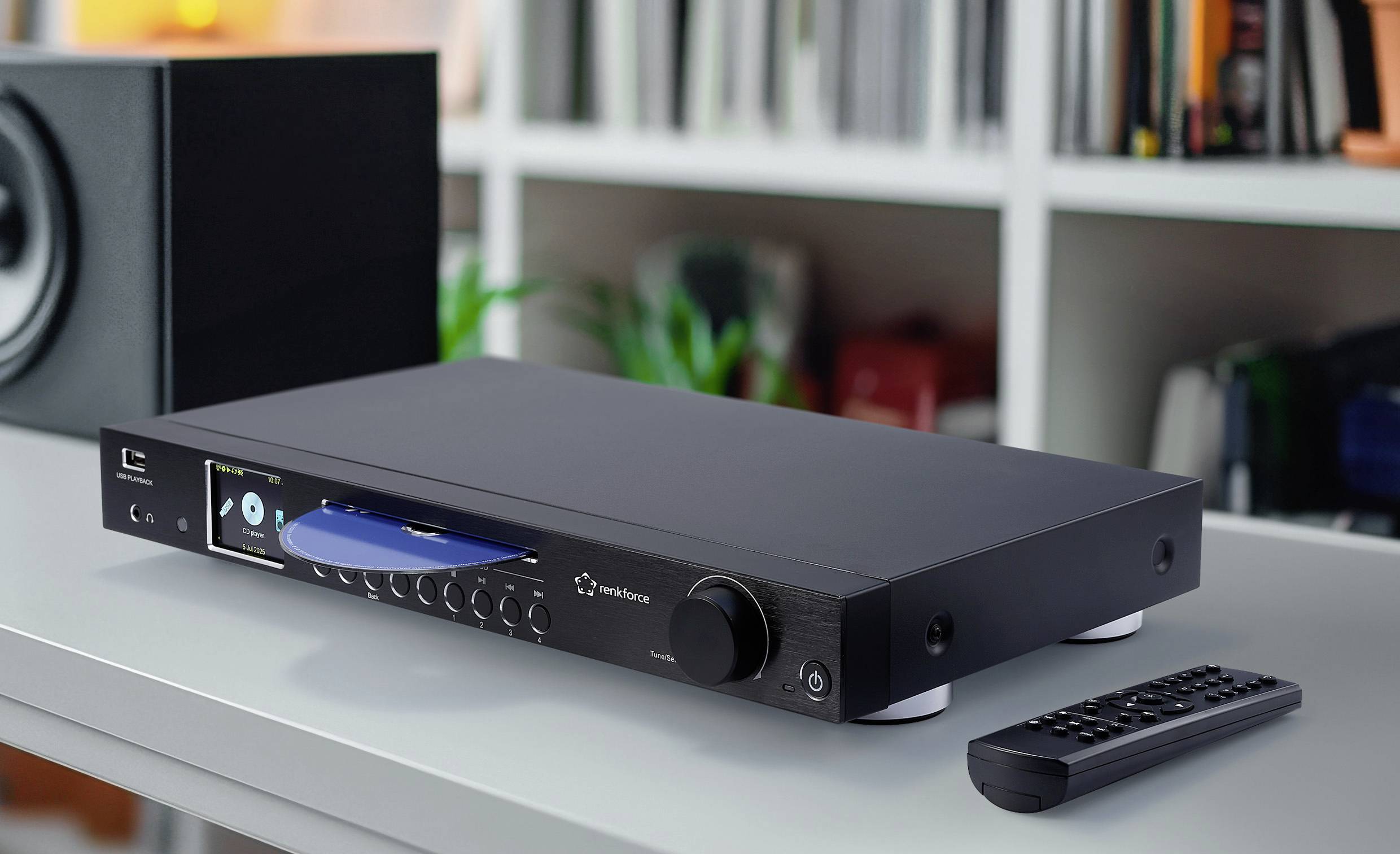 Elegantní audio CD přehrávač stojí na stole s dálkovým ovladačem v blízkosti. V pozadí jsou viditelné knihy na bílé police.