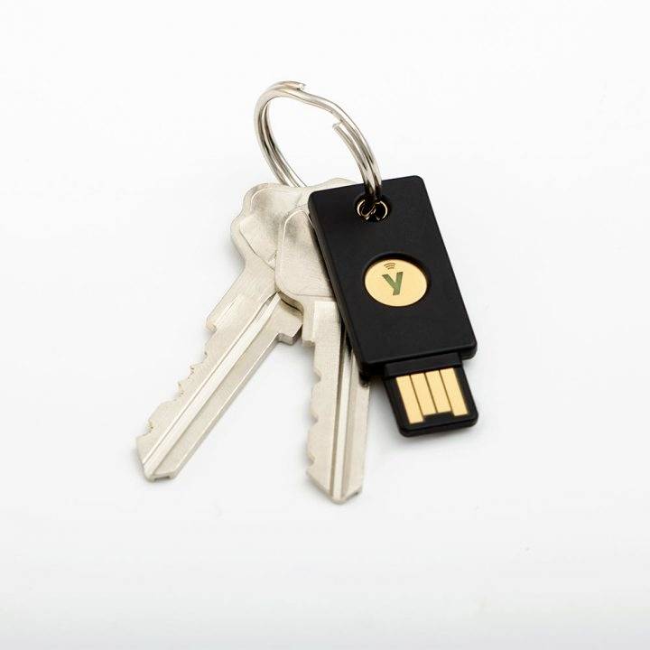 Dva stříbrné kovové klíče visí na klíčence vedle černého USB bezpečnostního klíče.