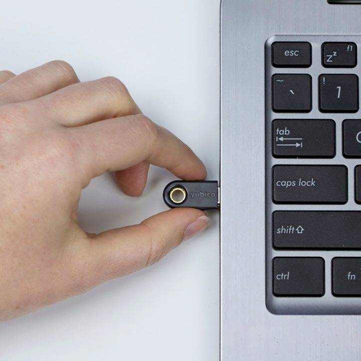 Ruka zasunuje bezpečnostní USB klíč do laptoptpu. Na klávesnici jsou viditelné klávesy jako 'esc' a 'caps lock'.