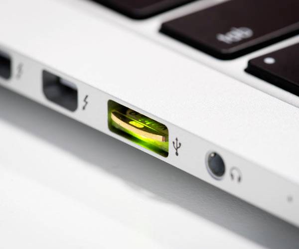 Detailní záběr USB flash disku zasunutého do notebooku. Flash disk svítí zeleně, což signalizuje, že je aktivní.