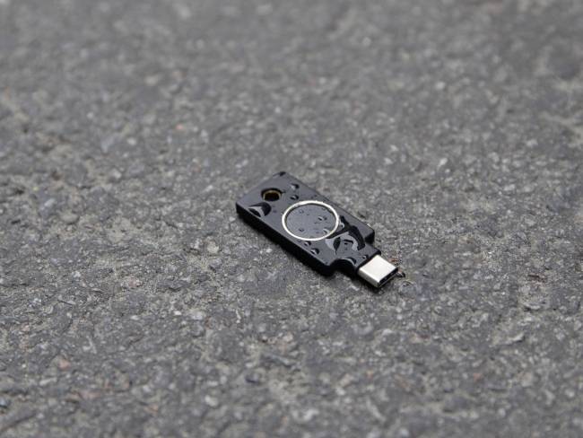 Malá elektronická součástka s USB-C konektorem leží na šedém asfaltovém povrchu.