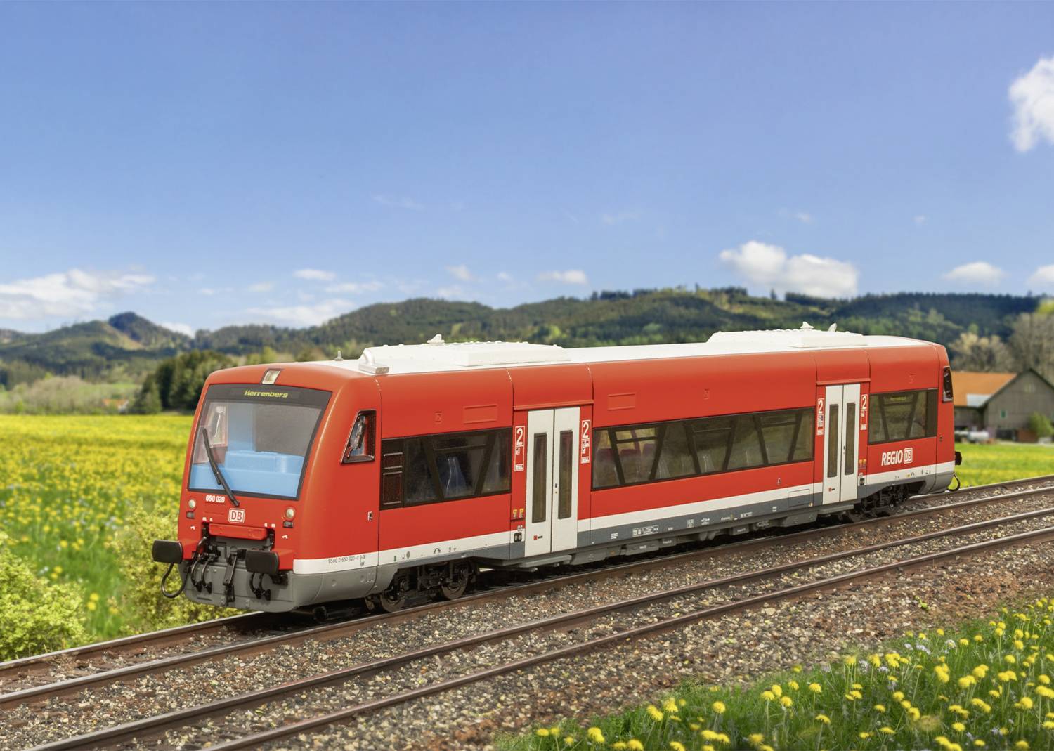Červený regionální vlak na venkovské železniční trati, obklopený zelenými loukami a kopci pod modrým nebem.