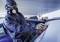 Osoba v ochranném oblečení a respirátoru brousí karoserii automobilu v dílně.