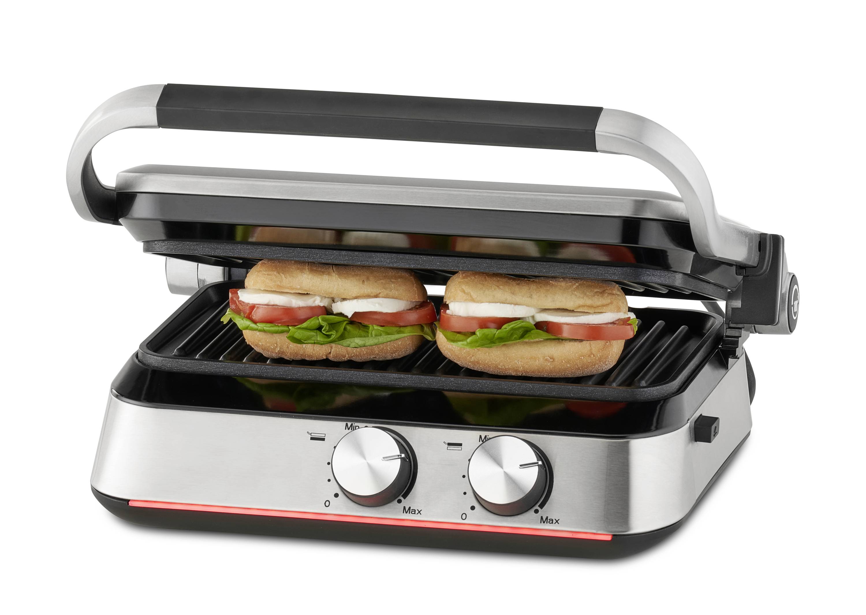 Stříbrný panini gril s otevřeným víkem. Na spodní grilovací desce leží dva panini s rajčaty, sýrem a salátem.