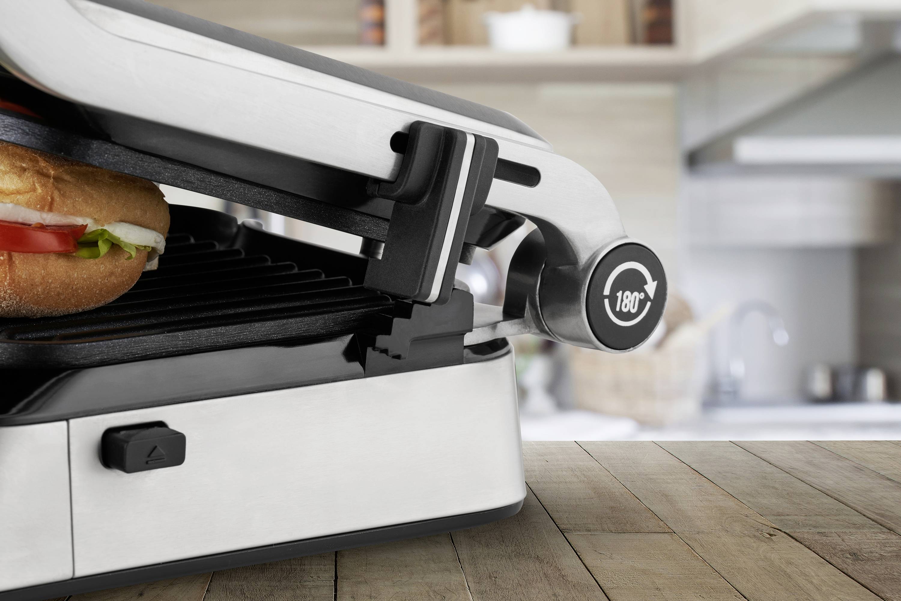 Sendvič se připravuje v elektrickém grilu v moderní kuchyni, teplotní regulátor ukazuje '180°'.