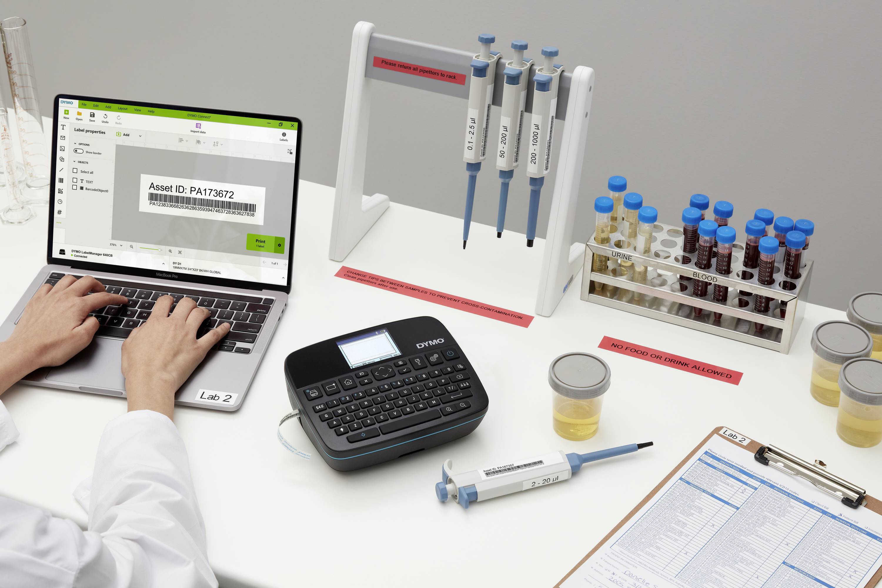 Laboratorní pracoviště s laptopem, tiskárnou štítků a biologickými vzorky. Jedna osoba zadává identifikační číslo do laptopu.