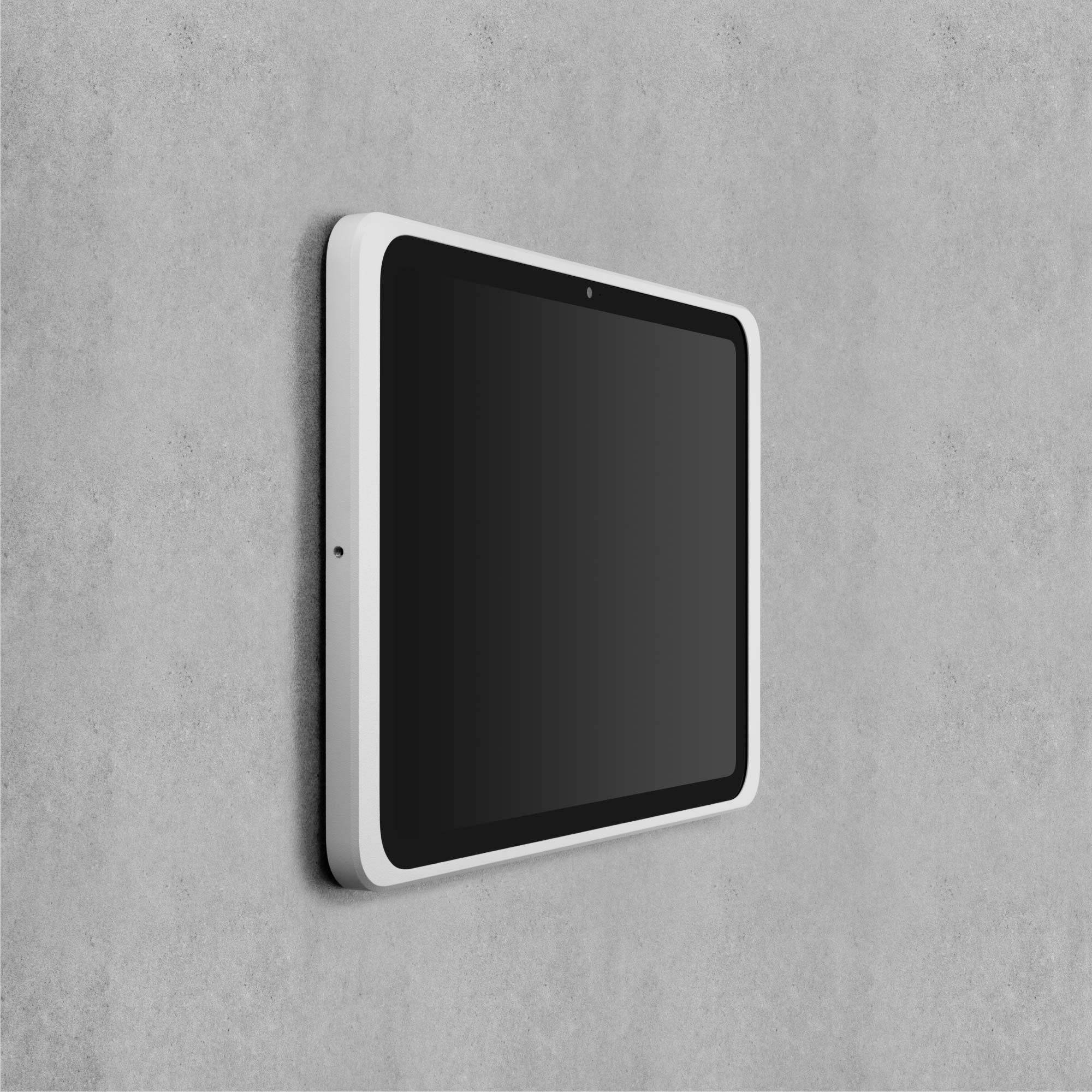 Bílý tablet je připevněn na šedé zdi. Obrazovka je vypnutá.