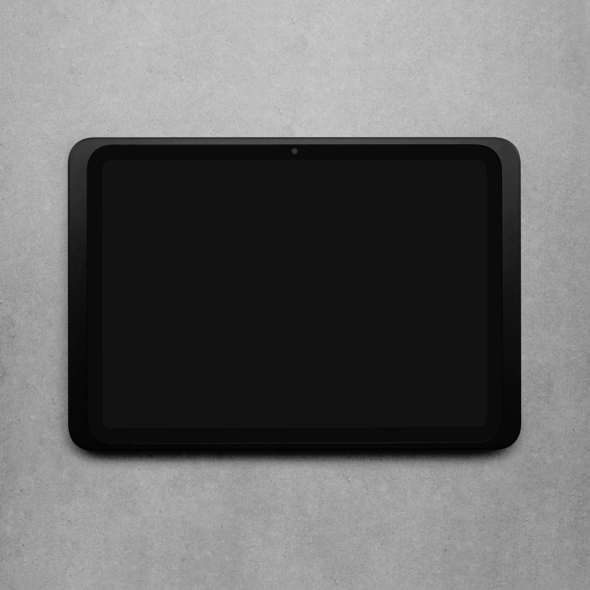 Černý tablet s velkým prázdným displejem leží plochým způsobem na šedém povrchu.