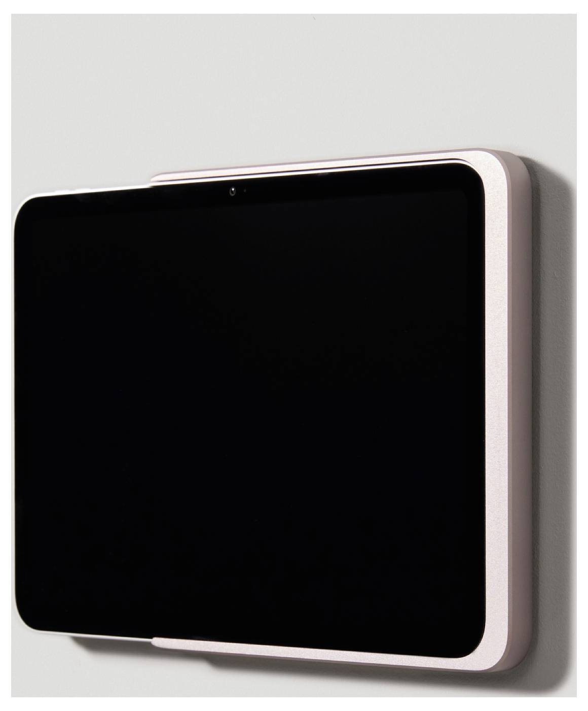 Tablet v růžovém obalu připevněný na světle šedé stěně. Obrazovka je černá, bez viditelného obsahu.