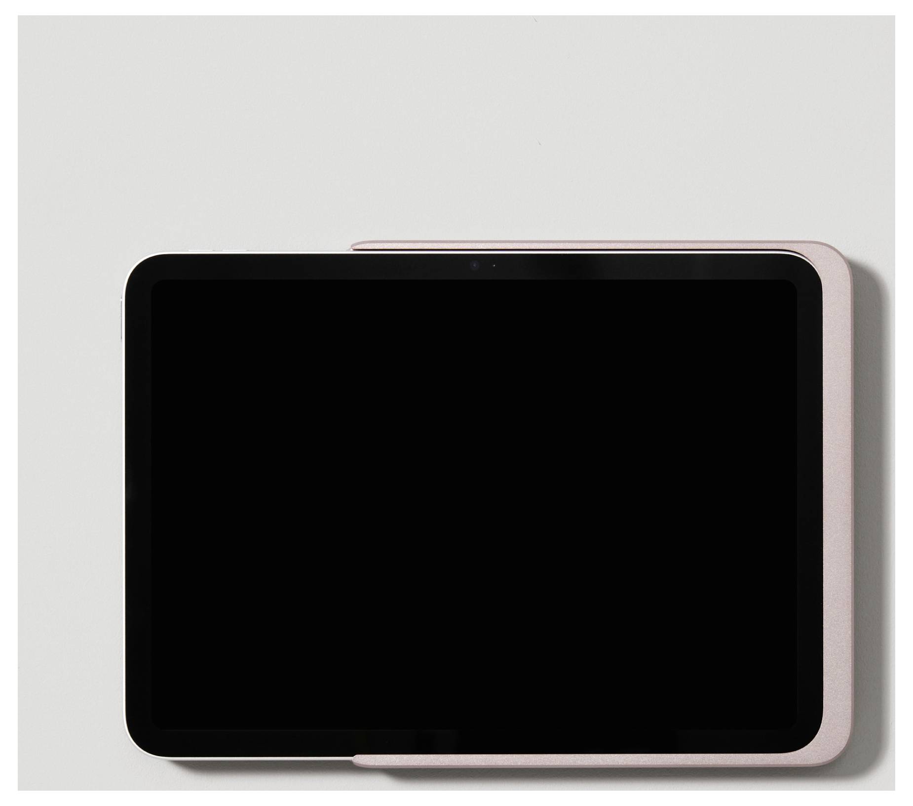Tablet s růžovým obalem na šedém pozadí.