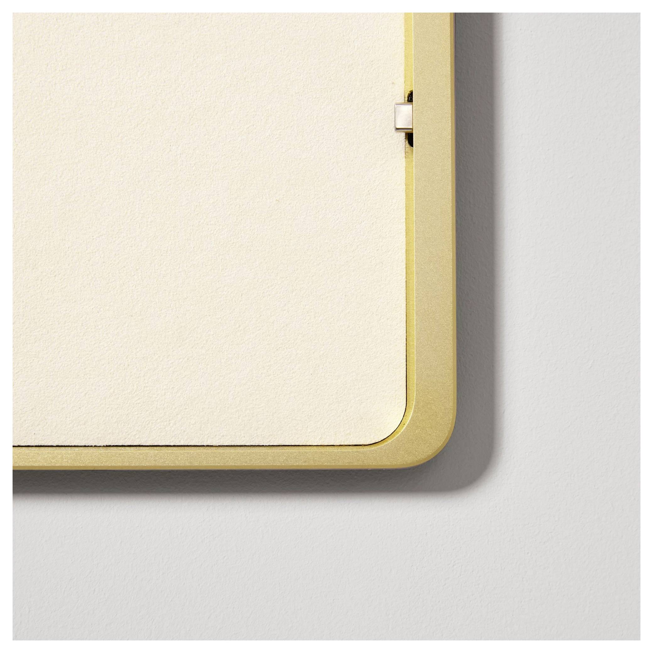 Roh zlatého obrazového rámu s tlumeně béžovým pozadím. Rám je připevněn na šedé stěně. Minimalistický design.