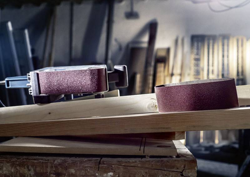 Bruska na pracovním stole s dřevěnými deskami v pozadí, zobrazující přípravu na řemeslné práce v dílně.