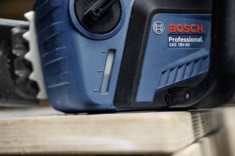 Detailní záběr modré elektrické řetězové pily značky 'BOSCH Professional' položené na dřevěném trámu.