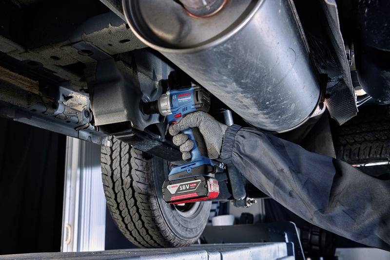 Mechanik v pracovním oblečení používá akumulátorový rázový utahovák, zatímco pracuje pod zdviženým vozidlem.