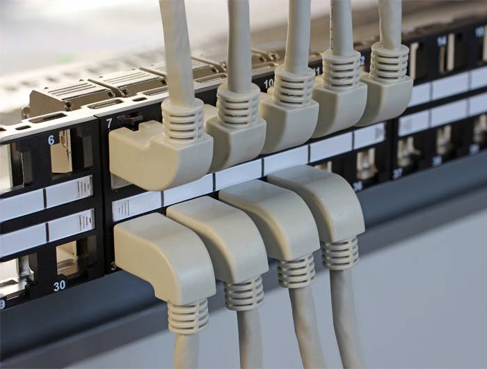 Síťové kabeláže: Několik ethernetových kabelů je zapojeno do číslovaných portů patch panelu, což představuje organizované datové propojení.
