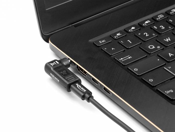 Je vidět černý notebook. Kabel je zapojen do HDMI portu. Klávesnice je částečně viditelná.