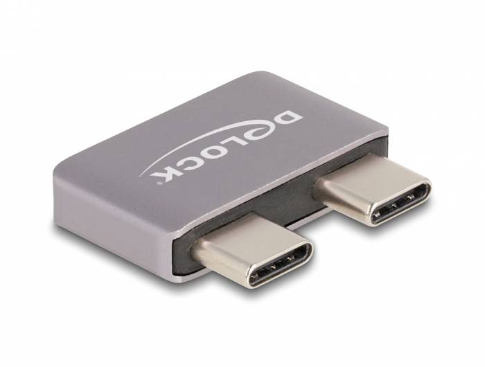 Adaptér se dvěma USB-C porty na jedné straně. Pouzdro je šedé a opatřené logem 'DE-LOCK'. Ideální pro připojení zařízení.