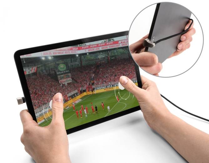 Osoba drží tablet, na kterém je vidět fotbalový zápas s přímým kopem. Tablet je připojen kabelem.