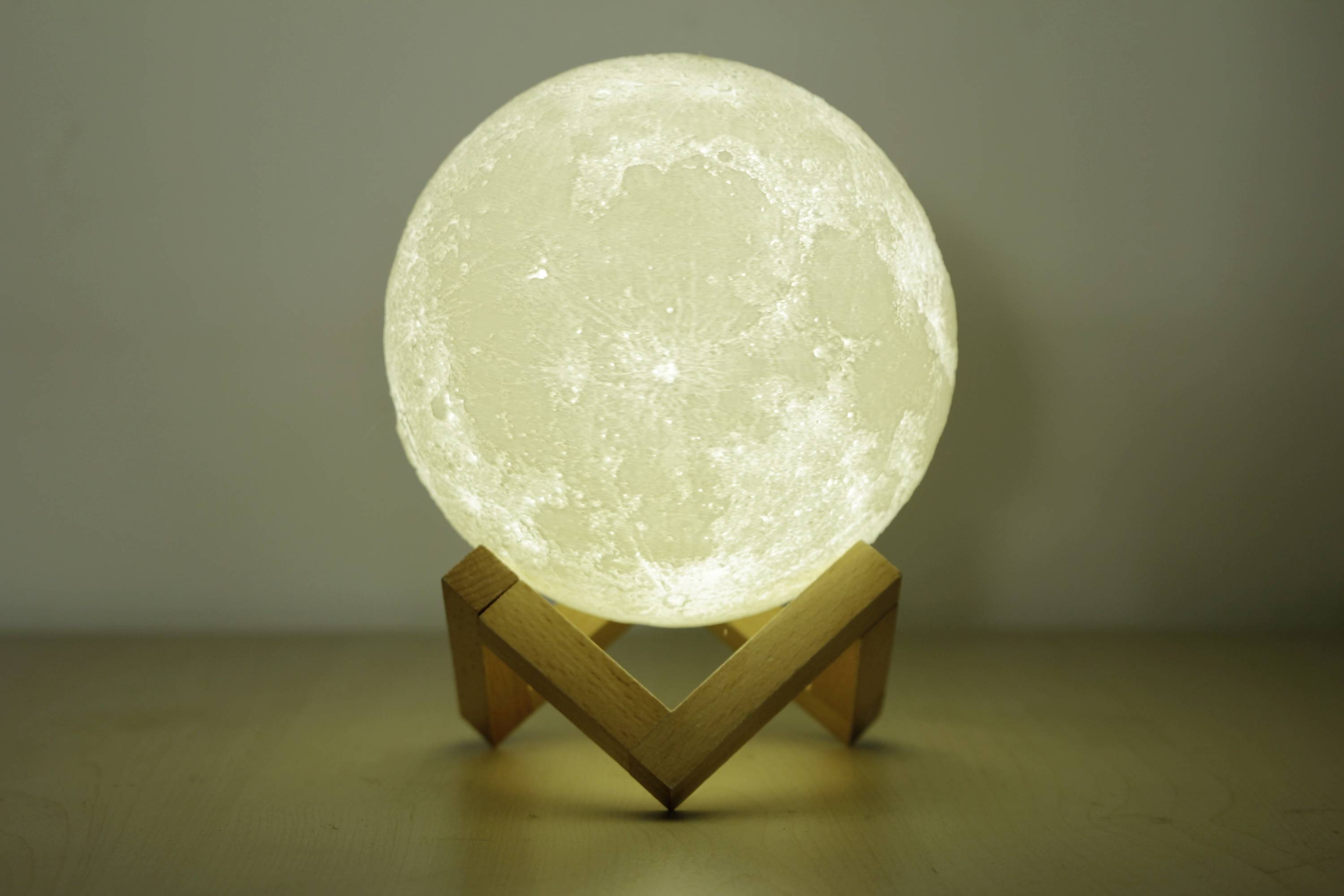Zářící měsíční lampa na dřevěném stojanu před šedým pozadím.