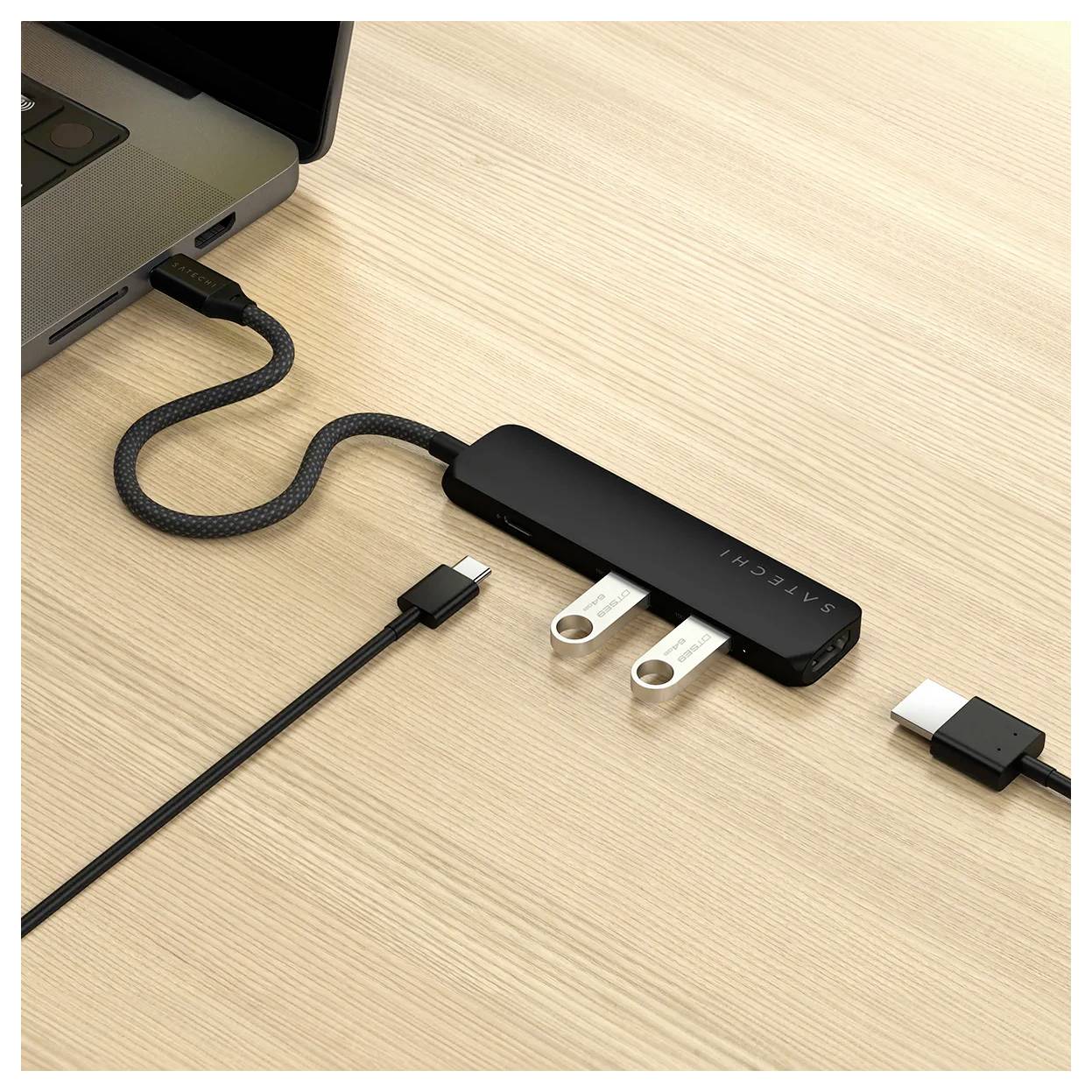 'Černý USB rozbočovač se dvěma zapojenými USB flashdisky je připojen k laptopu, který stojí na dřevěném stole.'