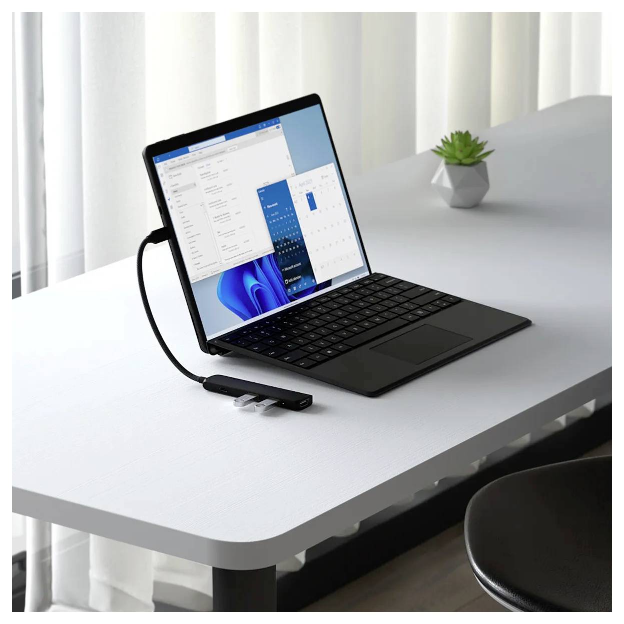 Laptop na stole, připojený k USB flash disku. V pozadí stojí malá rostlina na stole.