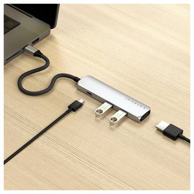 USB-C hub je připojen k laptopému počítači. Dva USB flash disky a kabel HDMI jsou připojeny k hubu. Hub leží na dřevěném stole.