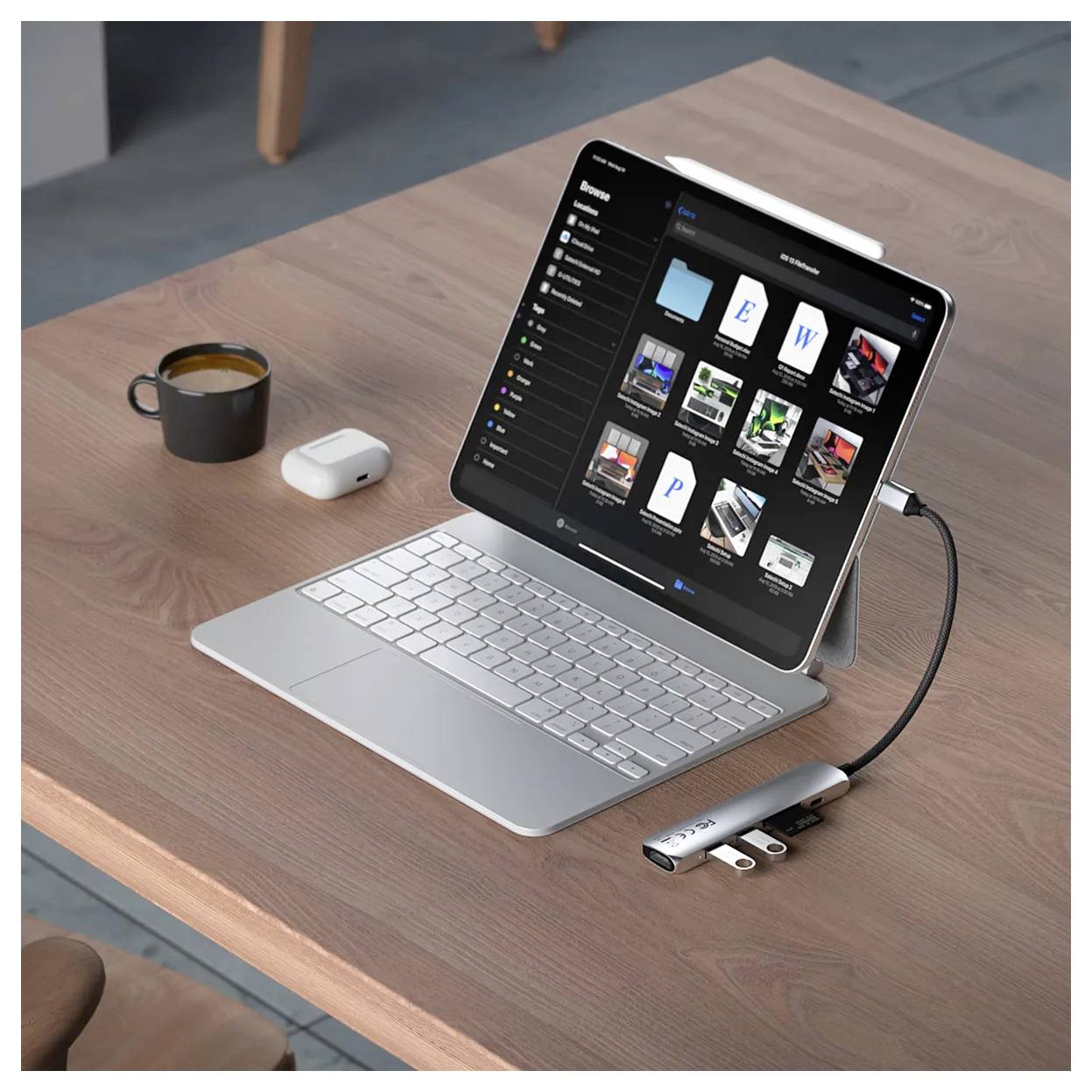 Tablet s klávesnicí leží na dřevěném stole. Zobrazuje správu souborů. Vedle je šálek, AirPods a dongle.