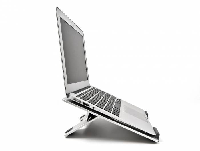 Na šikmém stojanu na notebook je umístěn stříbrný notebook, který zvedá úroveň obrazovky. Pozadí je jednotně bílé.
